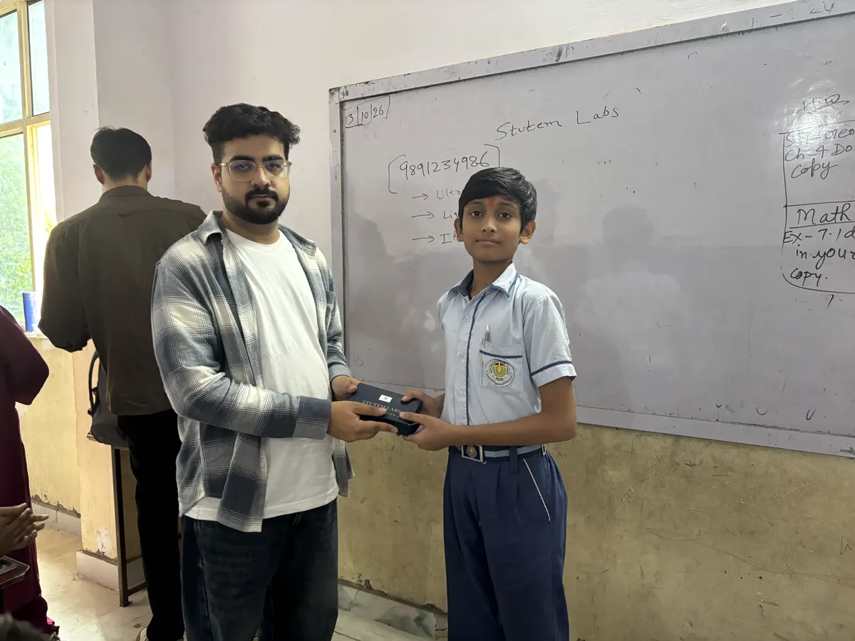 Mentor handing a StuTem kit to a student at the whiteboard