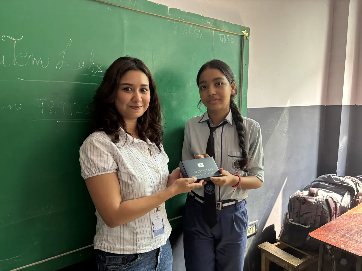 Mentor and student holding a StuTem kit in front of the chalkboard